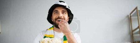 happy sports fan eating popcorn and watching championship at home, banner