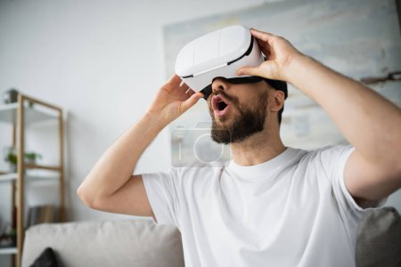 shocked bearded man adjusting vr headset while gaming at home