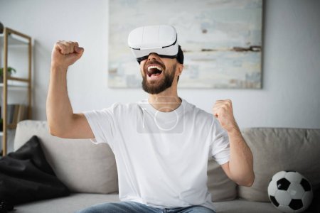amazed and bearded man in vr headset rejoicing while gaming in living room