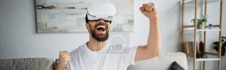 glücklicher und bärtiger Mann im vr-Headset jubelt beim Spielen im Wohnzimmer, Banner