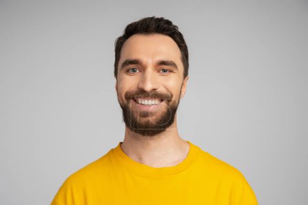 portrait of cheerful bearded man in bright yellow t-shirt looking at camera isolated on grey