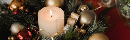 Christmas wreath with burning candle and shiny baubles and ribbon, banner