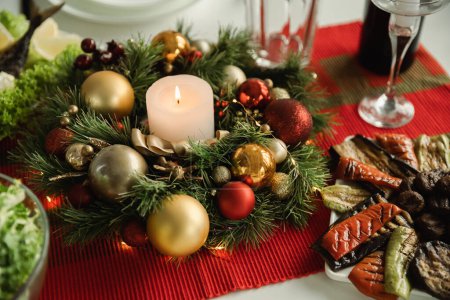 Christmas wreath with burning candle and baubles near grilled vegetables served for festive supper