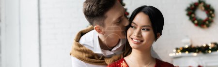 elegant asian woman smiling near husband kissing her on Christmas day, banner