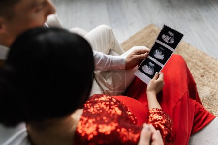 overhead view of man and woman in elegant clothes holding ultrasound scan with pregnancy confirmation 