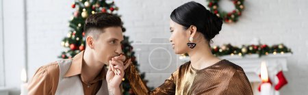 Photo for Young man kissing hand of elegant asian wife in living room during Christmas celebration, banner - Royalty Free Image