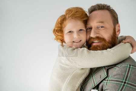 Téléchargez les photos : Garçon rousse positif en pull tricoté embrassant papa isolé sur gris - en image libre de droit