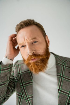 Photo for Portrait of stylish and bearded man touching hair and looking at camera isolated on grey - Royalty Free Image