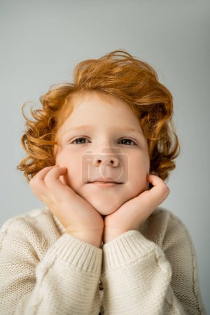 Photo for Redhead boy in warm beige jumper looking at camera isolated on grey - Royalty Free Image