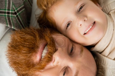 top view of cheerful bearded man with redhead son looking at camera
