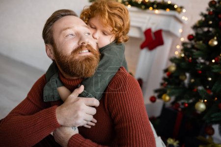 redhead child embracing happy bearded dad while celebrating Christmas at home