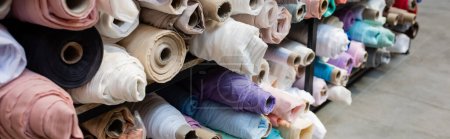 assortment of different fabric rolls on shelves in textile shop, banner
