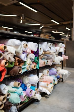 assortment of different fabric rolls on shelves in textile shop 