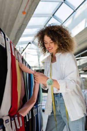 happy and curly saleswoman making choice from various fabric in textile shop