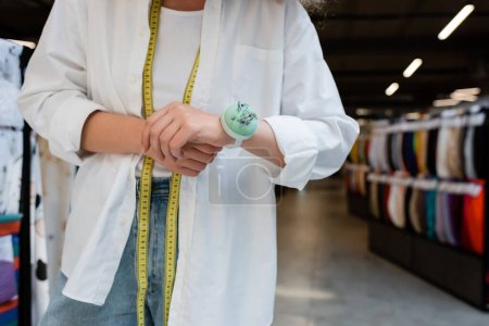 cropped view of saleswoman with measuring tape and needle cushion on hand in textile shop