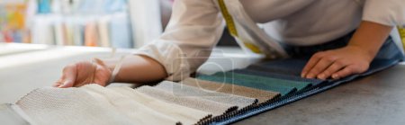partial view of blurred seller choosing among textile samples in shop, banner