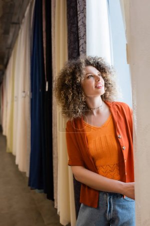 mujer joven feliz con el pelo rizado elegir nuevas cortinas en la tienda textil