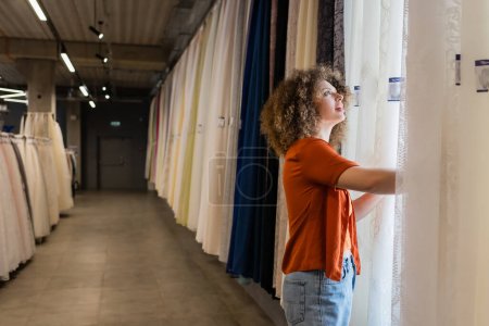 young amazed woman choosing looking at different curtains in textile shop