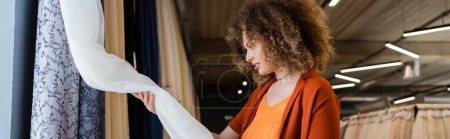 Photo for Side view of young woman looking at curtains in textile shop, banner - Royalty Free Image