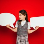 Girl in plaid skirt and vest holding white and empty speech bubbles isolated on red