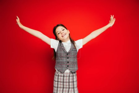 Photo for Cheerful girl in stylish checkered clothes standing with outstretched hands isolated on red, banner - Royalty Free Image