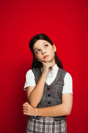 Photo for Dreamy girl in plaid vest holding hand near chin and looking away isolated on red, banner - Royalty Free Image