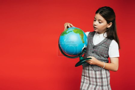 Preteen Schulmädchen in karierter Kleidung hält Globus isoliert auf rotem Banner 