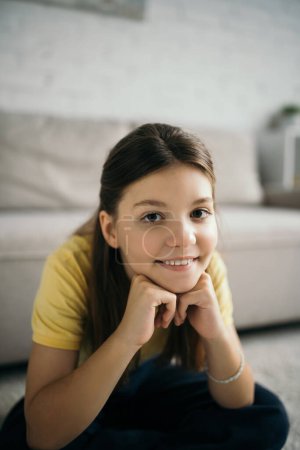 portrait of cheerful preteen girl sitting with hands near face and looking at camera