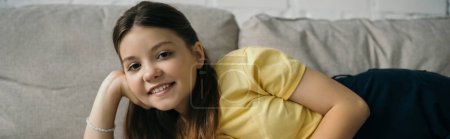 joyful girl relaxing on couch at home and smiling at camera, banner