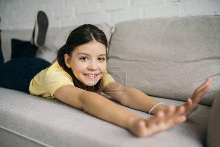 pleased girl looking at camera while stretching on comfortable sofa at home