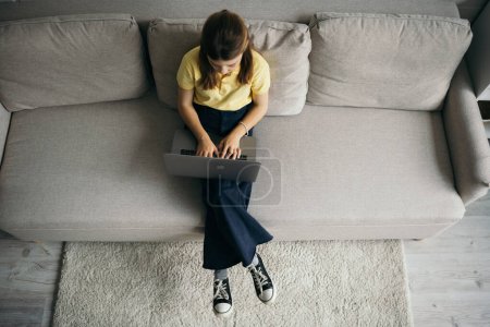 Photo for Top view of preteen girl using laptop on modern sofa at home - Royalty Free Image