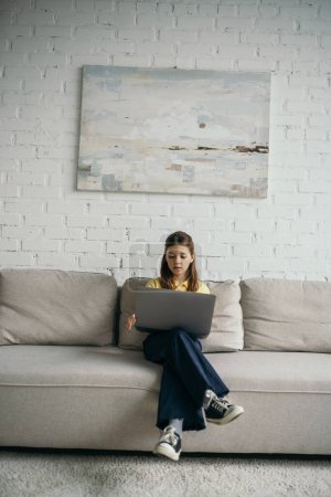 Foto de Longitud completa de la chica morena con el ordenador portátil sentado en acogedor sofá en la sala de estar - Imagen libre de derechos