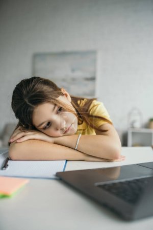 tired girl lying on table near notebook and laptop with blank screen at home