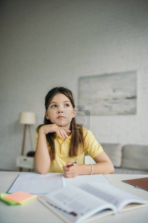 chica reflexiva sosteniendo la mano cerca de la barbilla y mirando hacia otro lado mientras hace la tarea