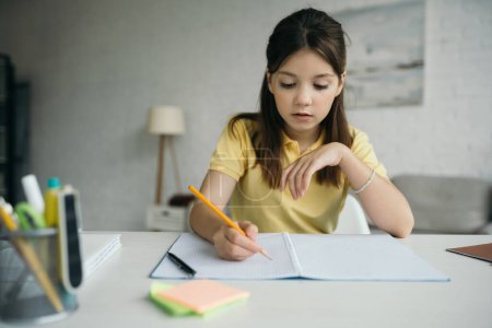 preteen girl with pencil writing in notebook on blurred foreground