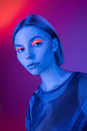 young woman with glowing makeup in blue neon light on purple and coral background
