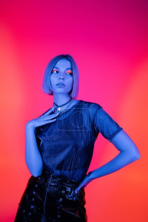 young and trendy woman posing with hand on hip in blue neon light on coral and pink background 