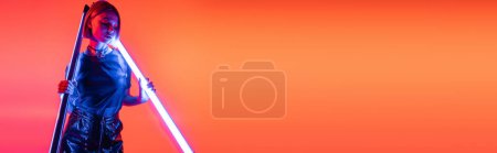 Photo for Trendy woman posing with fluorescent lamps on coral red background, banner - Royalty Free Image