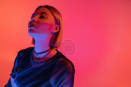 modische junge Frau schaut im Neonlicht auf rosa und korallenfarbenem Hintergrund weg