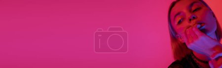 Téléchargez les photos : Femme avec néon maquillage tenant la main près du visage sur fond rose profond avec espace de copie, bannière - en image libre de droit