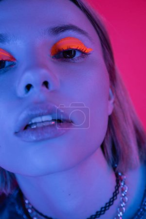 close up portrait of woman with bright neon eye shadow looking at camera in blue light on deep pink background