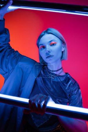 woman with neon makeup holding fluorescent lamps on coral and pink background 