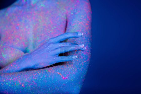 visión parcial de la mujer con manchas de neón brillantes en el cuerpo aislado en azul oscuro