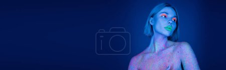mujer desnuda en brillante maquillaje de neón y pintura colorida salpicado mirando hacia otro lado sobre fondo azul oscuro, pancarta