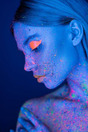 Photo for Profile of woman with vibrant makeup posing in neon light isolated on dark blue - Royalty Free Image