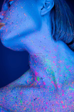 Téléchargez les photos : Vue rapprochée de la femme avec de la peinture au néon colorée sur le corps posant isolé sur bleu foncé - en image libre de droit