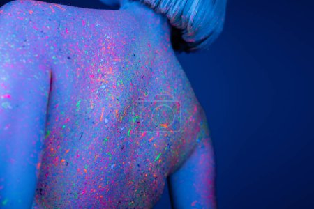 Téléchargez les photos : Vue arrière de la jeune femme avec éclaboussures lumineuses au néon sur le corps isolé sur bleu foncé - en image libre de droit