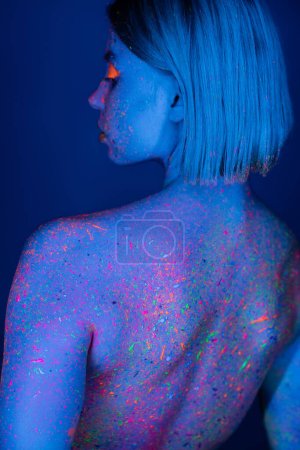 Rückansicht einer Frau mit leuchtenden Neon-Spritzern auf dem Körper isoliert auf dunkelblau