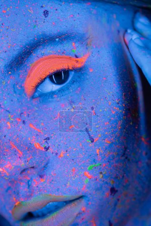 Téléchargez les photos : Vue rapprochée de la femme recadrée avec fard à paupières corail vibrant et peinture au néon sur le visage - en image libre de droit
