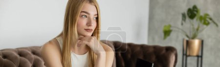 Mujer bastante joven mirando hacia otro lado mientras está sentado en el sofá en casa, pancarta 